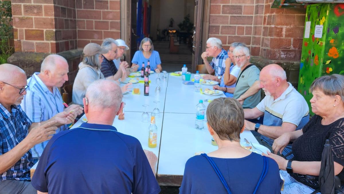 Menschen sitzen an einer langen Tafel vor der Kirche und essen gemeinsam im Freien.
